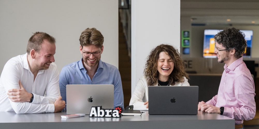 Four Abra colleagues laughing together around a conference table